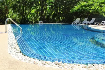 a large blue swimming pool with chairs and trees at Patong Palace Hotel - SHA Extra Plus in Patong Beach
