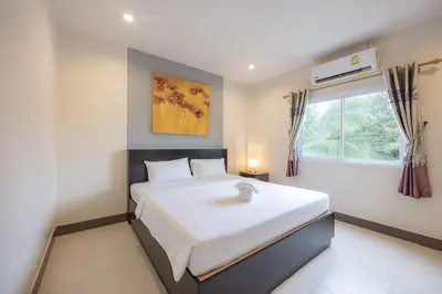a bedroom with a large white bed and a window at Baan Yuyen Karon Guesthouse in Karon Beach