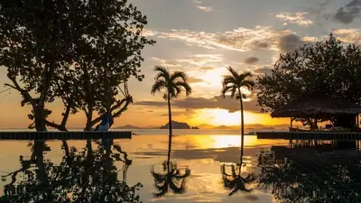 a pool with palm trees and a sunset in the background at Yao Yai Beach Resort in Ko Yao Yai