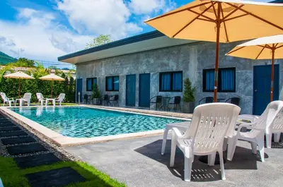 a pool with chairs and umbrellas next to a house at Ongsa House in Bang Tao Beach