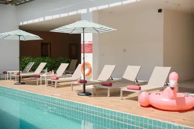 a pool with chairs and umbrellas next to a swimming pool at Nonnee Hotel Kata Beach Phuket in Kata Beach