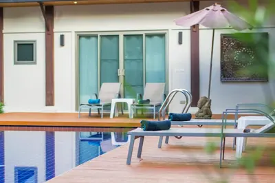 a patio with chairs and an umbrella next to a pool at Emerald Pool Villa Lush Villa On A Sunny Island in Nai Harn Beach