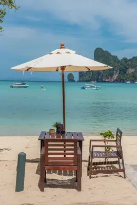 a table and chairs under an umbrella on the beach at PP Charlie Beach Resort in Phi Phi Don