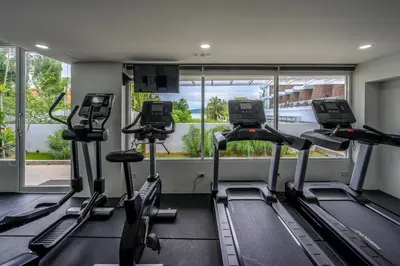 a gym with treadmills and ellipticals in front of a window at The Beachfront Hotel Phuket in Rawai Beach