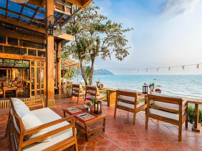 an outdoor patio with chairs and tables and the ocean at Santhiya Koh Yao Yai Resort & Spa - Compulsory Join Santhiya Speedboat from-to Ao Po Grand Marina at Phuket in Ko Yao Yai