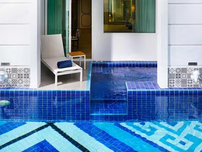 a pool with a blue tile floor and a chair at Mövenpick Myth Hotel Patong Phuket in Patong Beach