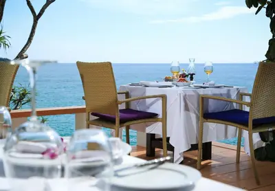 a table with chairs and wine glasses and the ocean at Mom Tri's Villa Royale - SHA Plus in Kata Beach