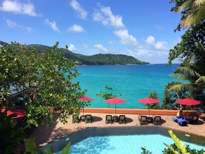 a swimming pool with chairs and umbrellas and the ocean at Mom Tri's Villa Royale - SHA Plus in Kata Beach