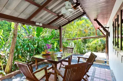 a patio with a wooden table and chairs and trees at Thai Style 2BR Villa Nikkie 2 in Nai Harn Beach