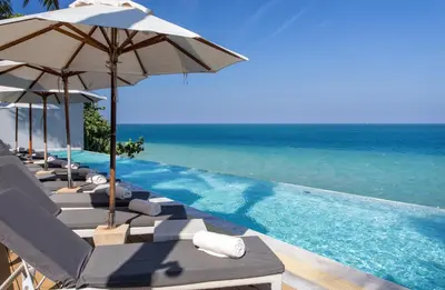 a pool with chairs and umbrellas and the ocean at Cape Sienna Phuket Gourmet Hotel & Villas - SHA Extra Plus in Kamala Beach
