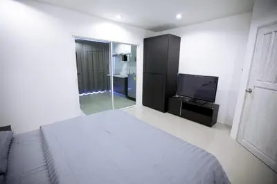 a white bedroom with a bed and a television at Number 4 Phuket in Nai Harn Beach