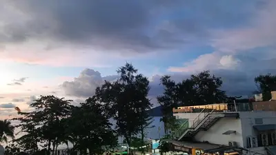 a cloudy sky with trees in front of a building at Big Boys' Bed & Burger - Patong Beach in Patong Beach