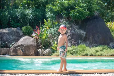 a young boy standing on a surfboard in a pool at Roost Glamping - SHA Certified in Rawai Beach