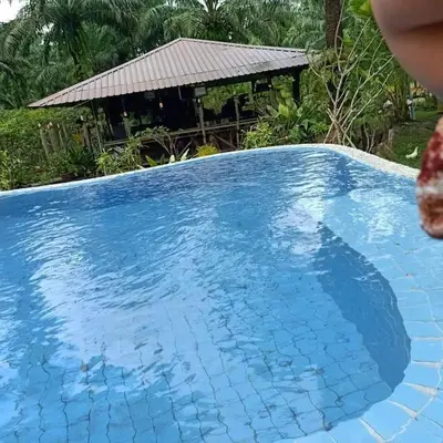 a large blue swimming pool with a house in the background at Koom Kachanaan in Ban Nong Thale