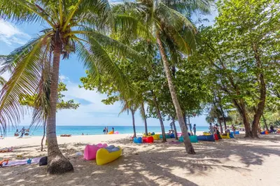 a beach with palm trees and people on the beach at The Palmyrah Surin by Holy Cow, 1-BR, courtyard or pool view in Surin Beach