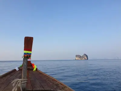 a boat in the water with a rock in the distance at Aladdin Guest House in Phi Phi Don