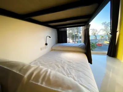 a bed in a room with a large window at Fishtail Hostel Phuket in Karon Beach