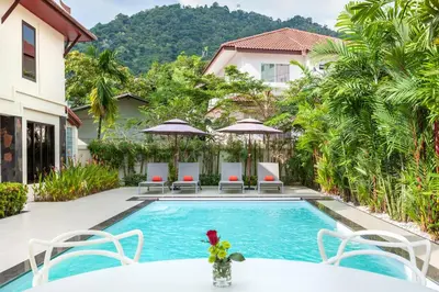 a pool with chairs and tables and a house at Sabai Villa Kata by RESAVA in Kata Beach
