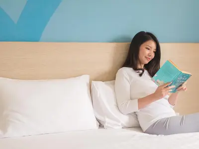 a woman sitting on a bed reading a book at HOP INN Phuket Old Town in Phuket Town