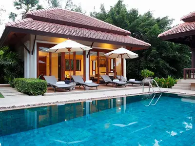 a swimming pool with chairs and umbrellas next to a house at Laguna Waters in Phuket Town