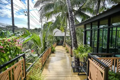 a wooden walkway through a garden with palm trees at Dee Homestay in Ban Pa Khlok