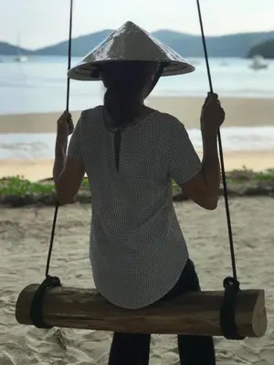 a woman wearing a hat sitting on a bench on the beach at The Mooring Resort in Panwa Beach