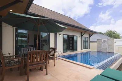 a patio with chairs and an umbrella next to a swimming pool at Foxtail Palm Villa in Rawai Beach