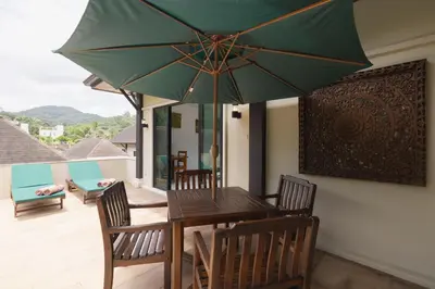 a wooden table with chairs and a green umbrella at Cocktail Palm Villa in Rawai Beach