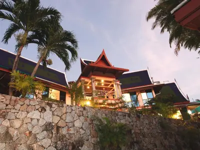 a building with palm trees and a stone wall at Kata Sea View Villas in Kata Beach