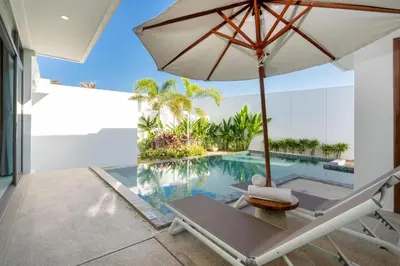 an umbrella and a chair next to a swimming pool at Shambhala Grand Villa - Private Pool Villas by Escape Villas - Top Choice - Guest Favorite - Best Location in Bang Tao Beach