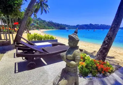a statue next to a beach with a chair and flowers at Mango Tree Villa in Panwa Beach