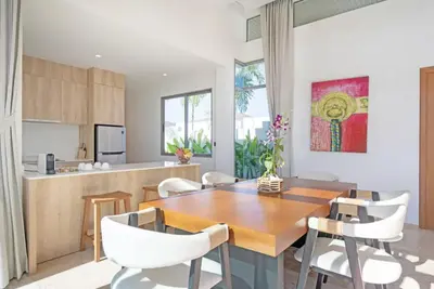 a kitchen and dining room with a wooden table and white chairs at SHAMBHALA GRAND Pool Villas x MonthStayZ Thailand in Phuket Town