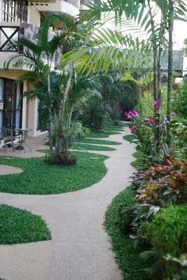 a walkway in a garden with palm trees and plants at Sunset Apartment Phuket in Patong Beach