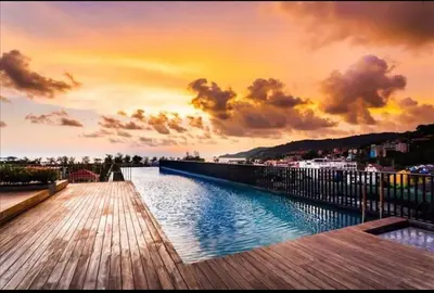 a wooden walkway leading to a pool with a sunset at The Deck Patong in Patong Beach