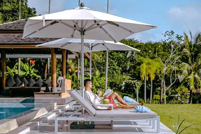 a man sitting in a chair under an umbrella next to a pool at VILLA DIVA STAR in Ko Yao Noi