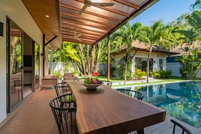 an outdoor dining area with a wooden table and chairs and a pool at villa Akala in Ban Saiyuan (1)