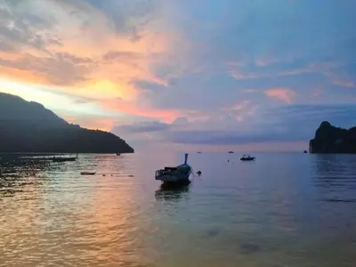 a boat sitting in the water at sunset at Dalum Beachhouse in Phi Phi Don