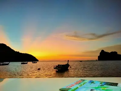 a sunset over the water with a boat in the ocean at Dalum Beachhouse in Phi Phi Don