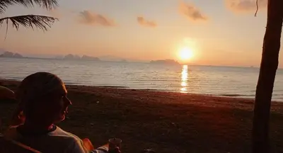 a woman sitting on the beach watching the sunset at Koh Yao Noi Beach Resort in Ko Yao Noi