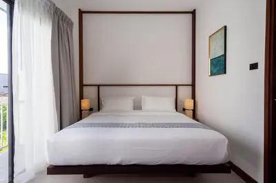 a bedroom with a white bed with a large window at Baan Kamana Guest House in Phangnga