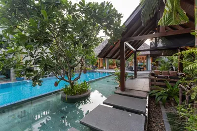 a swimming pool next to a house with a tree at Stunning 5BR villa with freshwater pool & tropical garden in Ban Phru Champa