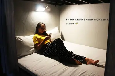 a woman sitting on a bed looking at her cell phone at Beehive Phuket Old Town Hostel in Phuket Town