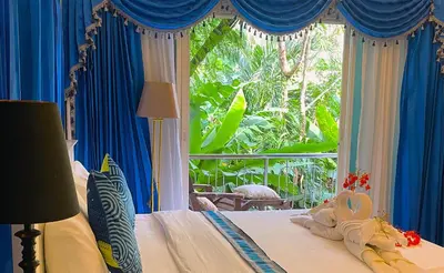 a bedroom with a bed with blue curtains and a window at OASIS VILLA Karon Beach in Karon Beach