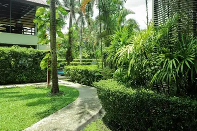 a path through a garden with palm trees and a building at Casuarina Shores Apartment - SHA Plus in Bang Tao Beach