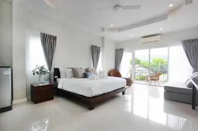 a white bedroom with a bed and a large window at The Langstan Suites in Nai Harn Beach