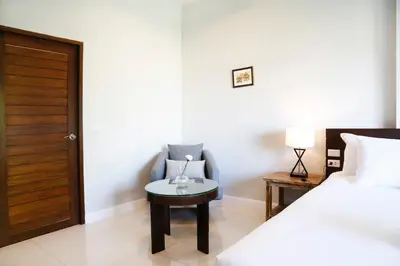 a bedroom with a bed and a chair and a table at The Langstan Suites in Nai Harn Beach