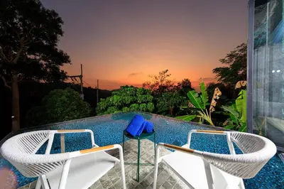 two chairs and a pool with a sunset in the background at Romantic villa in the tropics near Kamala Beach in Kamala Beach