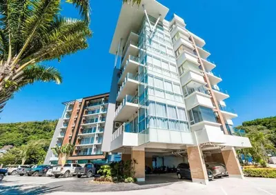 a tall white building with cars parked in a parking lot at Chic Condominium by Redfox Hospitality in Karon Beach