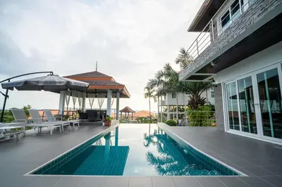 a swimming pool with chairs and an umbrella next to a house at ฺBaan Waru seaview villa in Kata Beach