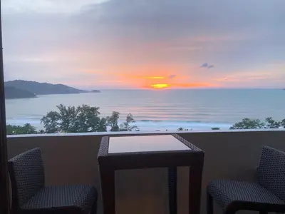 a view of a sunset from a balcony with chairs and a table at Patong Tower Ocean View Apartment in Patong Beach